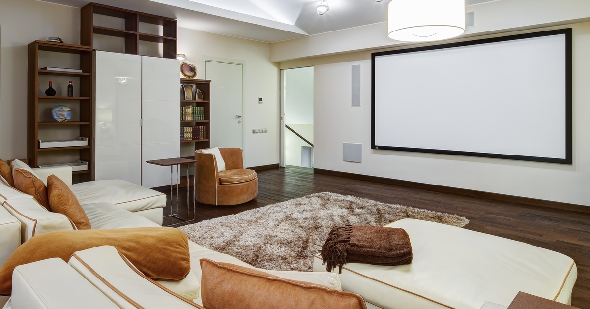 A cozy white and beige home theater with different shades of brown accents, shelving, rugs, and blankets.