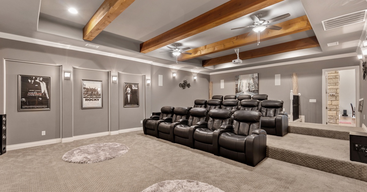 A large carpeted, at-home theater with rows of black leather recliners, with black and white movie posters on the wall.