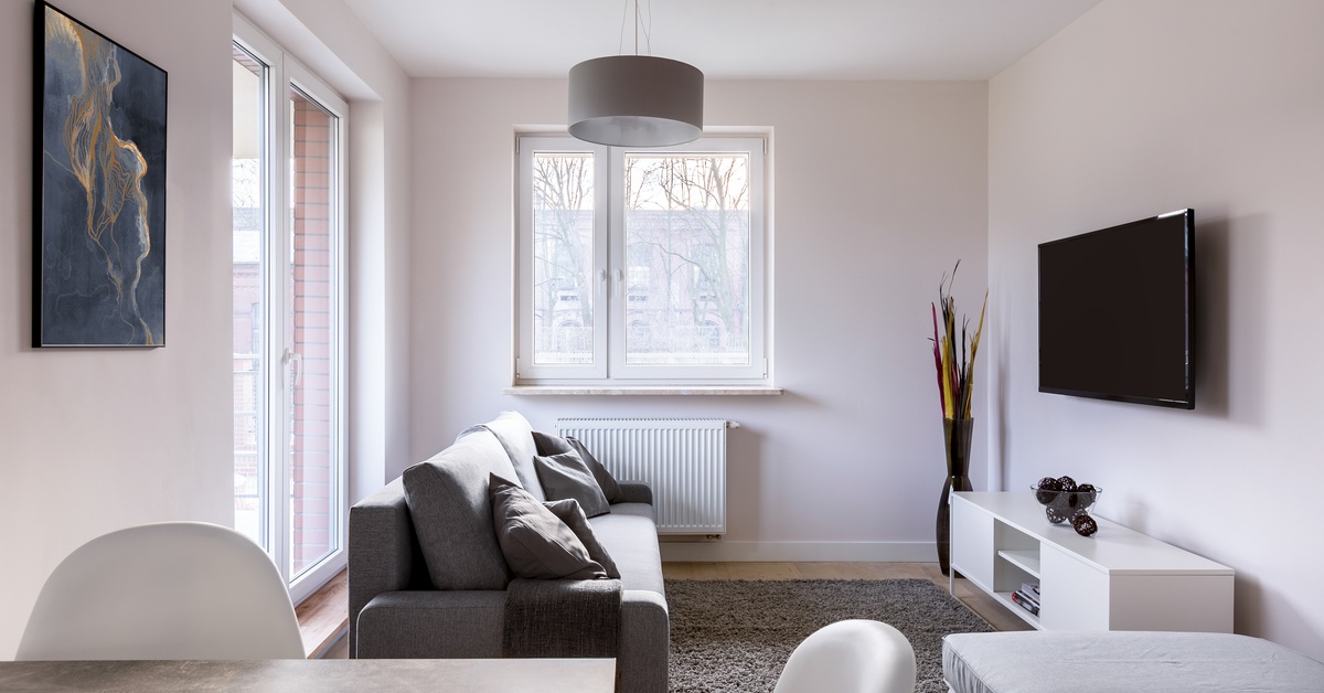 A modern gray interior of a small living room, including a couch, a small wall-mounted television, and a breakfast nook.