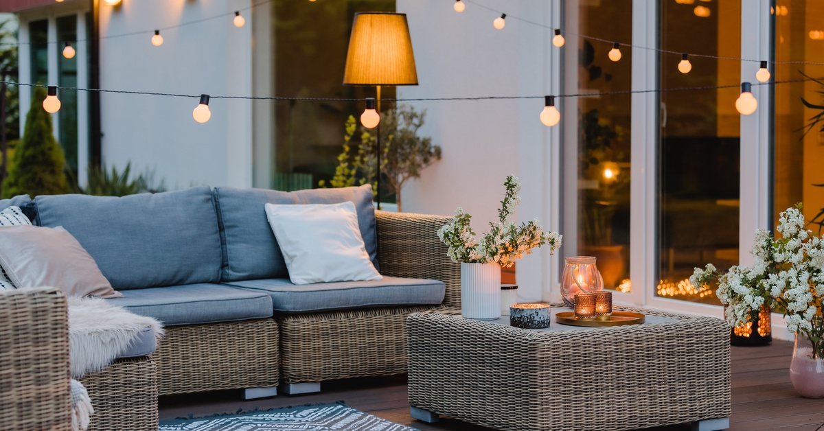Gray rattan outdoor furniture with blue cushions is decorated with white flowers, sitting under the glow of fairy lights.