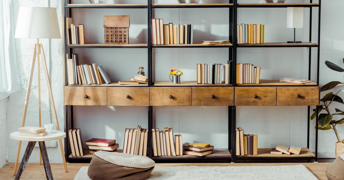 A close-up of a large bookshelf with a metal structure and wooden drawers, full of books in front of a white wall.