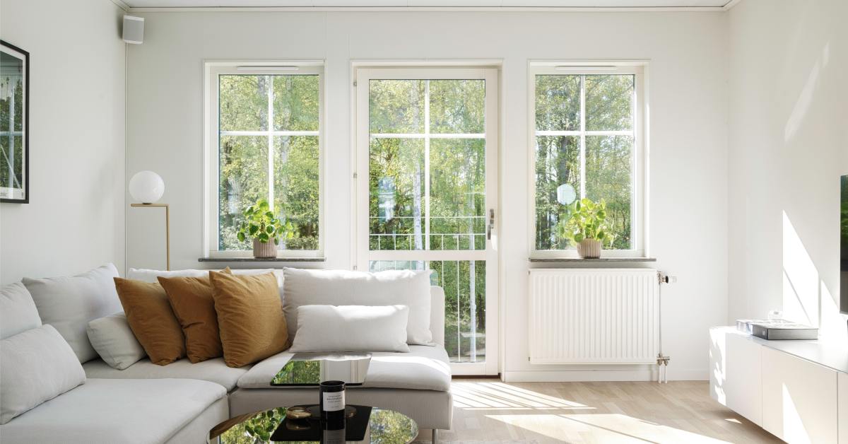 A living room with a small area rug, a white sectional couch, large windows with small plants, and a glass door.