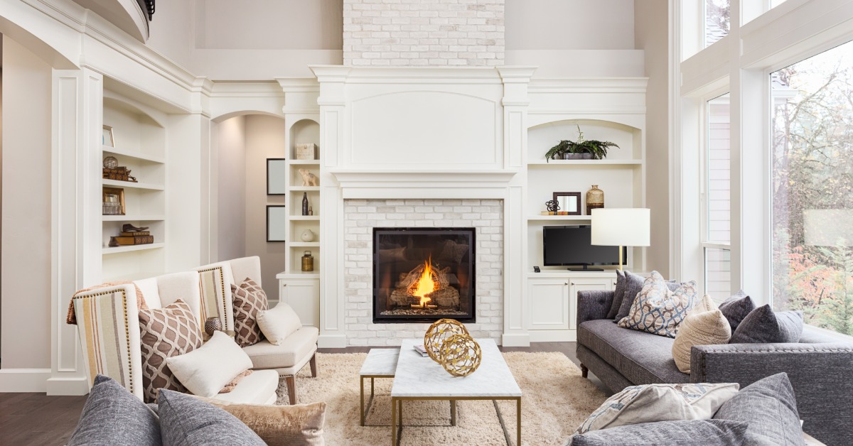 A cozy living room with white walls and a brick chimney, two grey couches, two white chairs, and a coffee table.