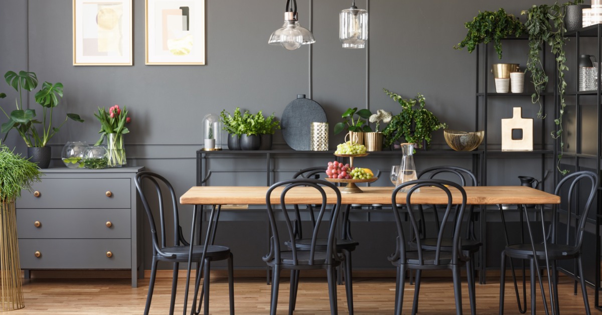 A rectangular dining table with metal chairs in a room with wooden floors, grey walls, and grey furniture with plants.