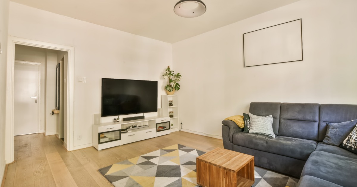 A white entertainment console next to a white wall holding a flat screen in a room with a sectional couch and a rug.